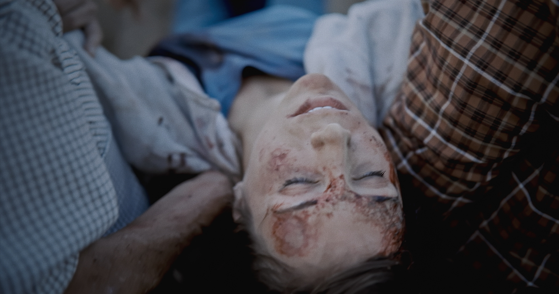 Close up on a woman's face covered in dirt as she lays on her back, held by two people