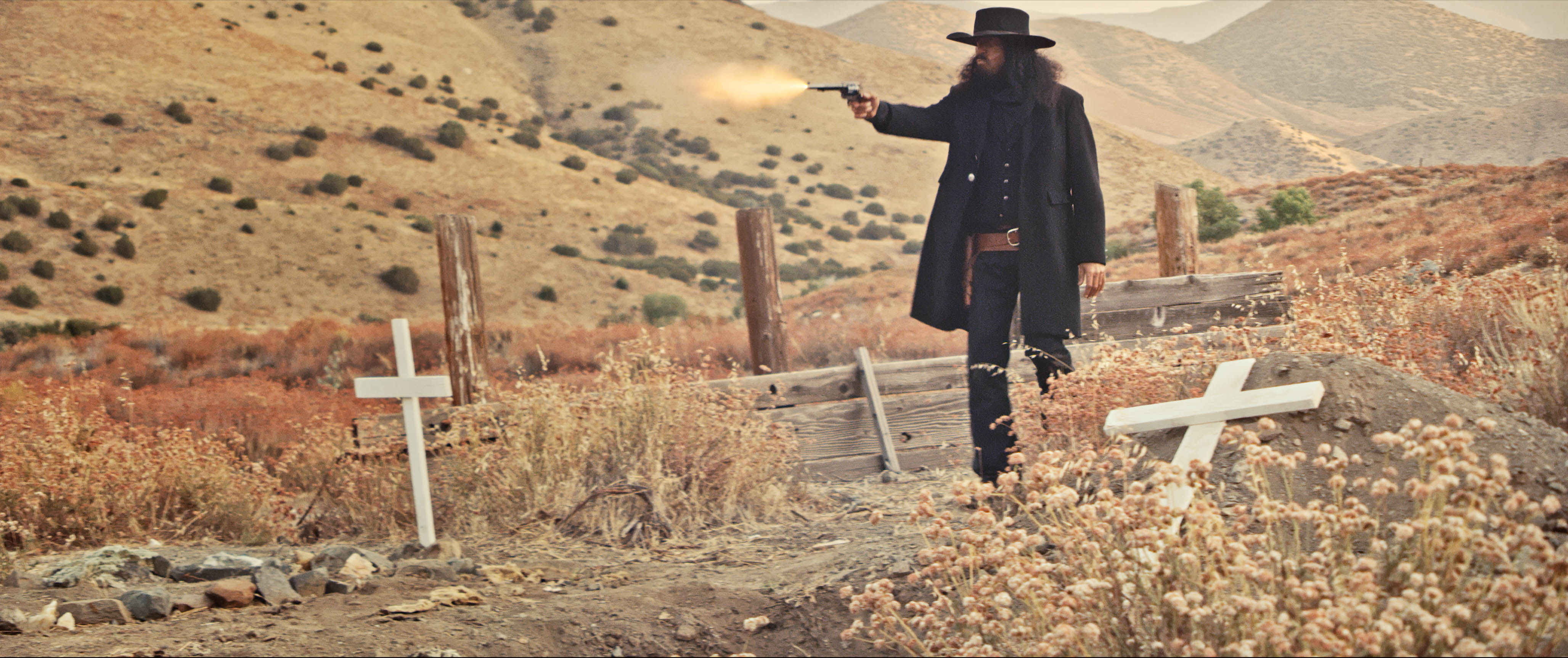 A man fires a pistol while in a graveyard